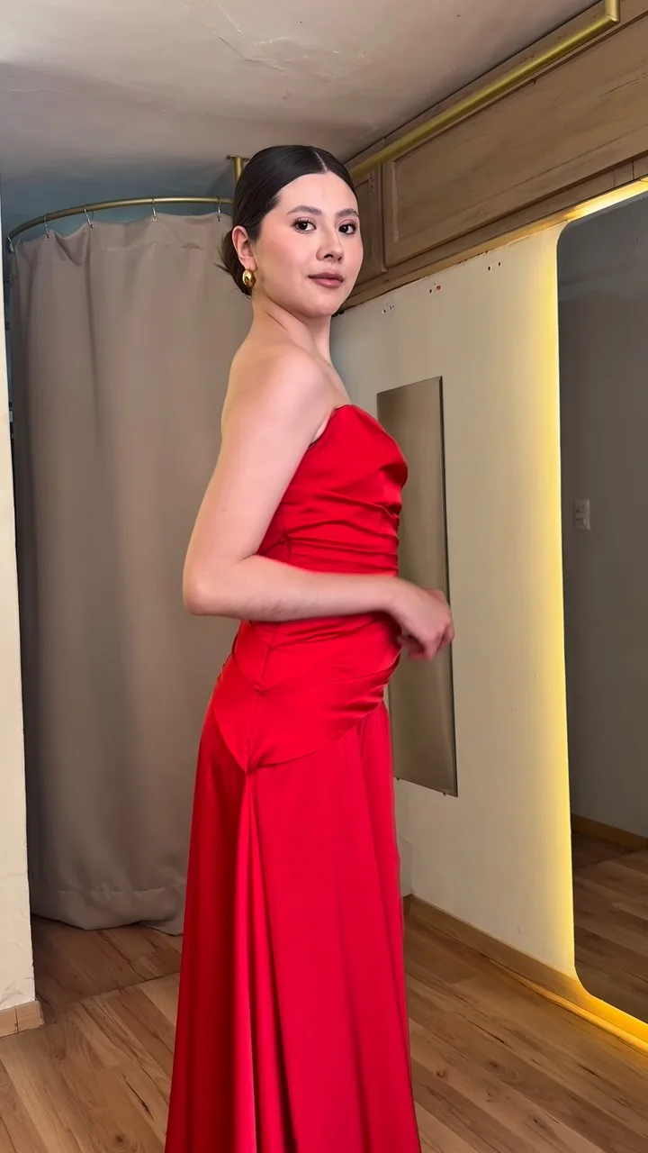 Una modelo de perfil con vestido largo rojo de satén, sin tirantes, en el probador de HIMALIA