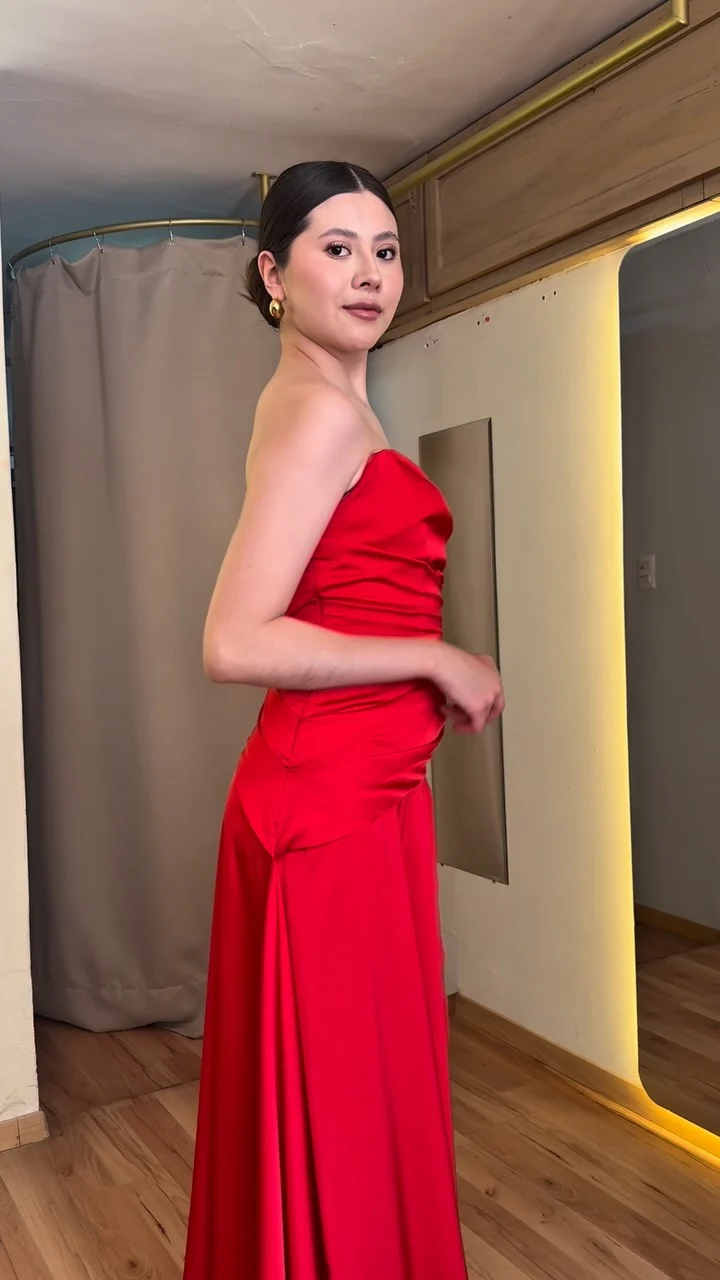 Una modelo de perfil con vestido largo rojo de satén, sin tirantes, en el probador de HIMALIA