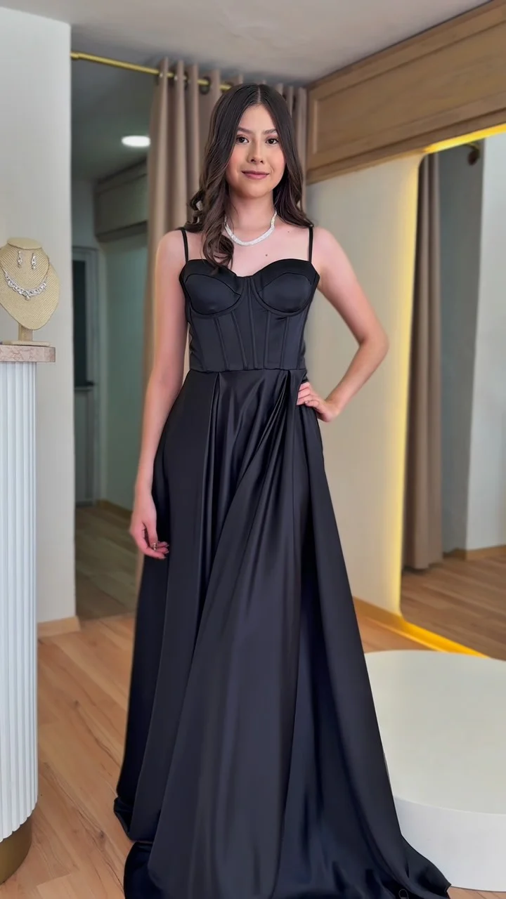 Una modelo con vestido largo negro de satén, con corsé y tirantes delgados, en el probador de HIMALIA